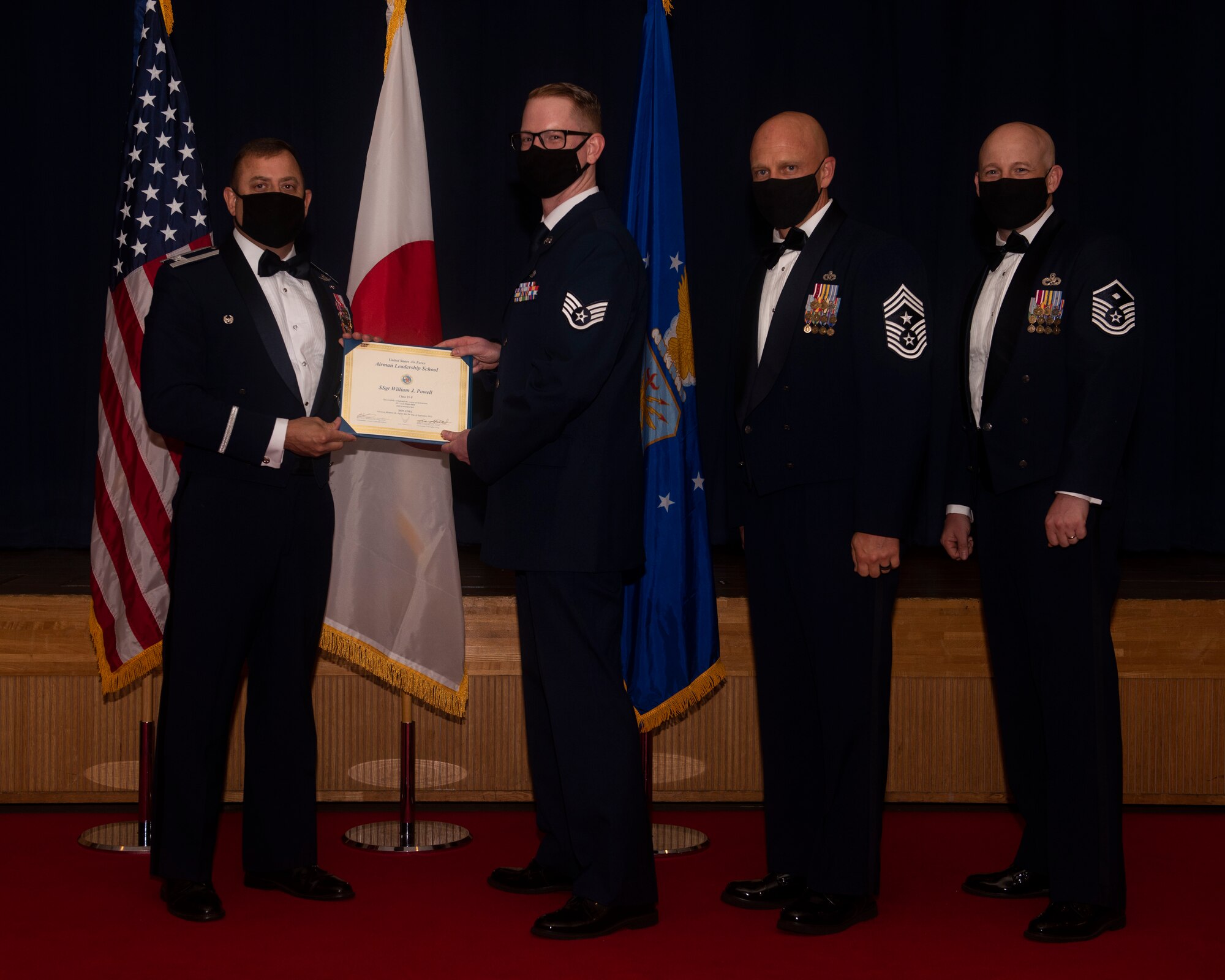 Military members in uniform pose with a diploma for a photo