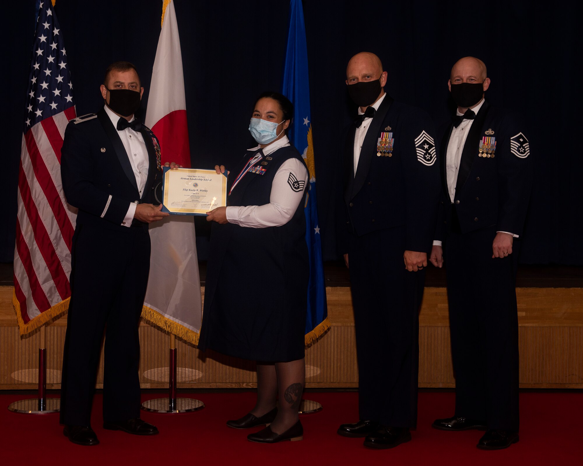 Military members in uniform pose with a diploma for a photo
