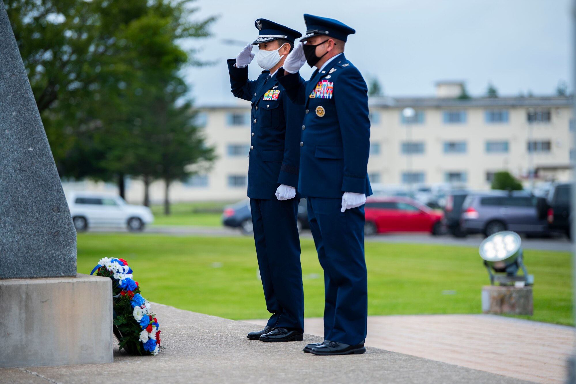 Military member in uniform salute to a wreath placed on the ground.