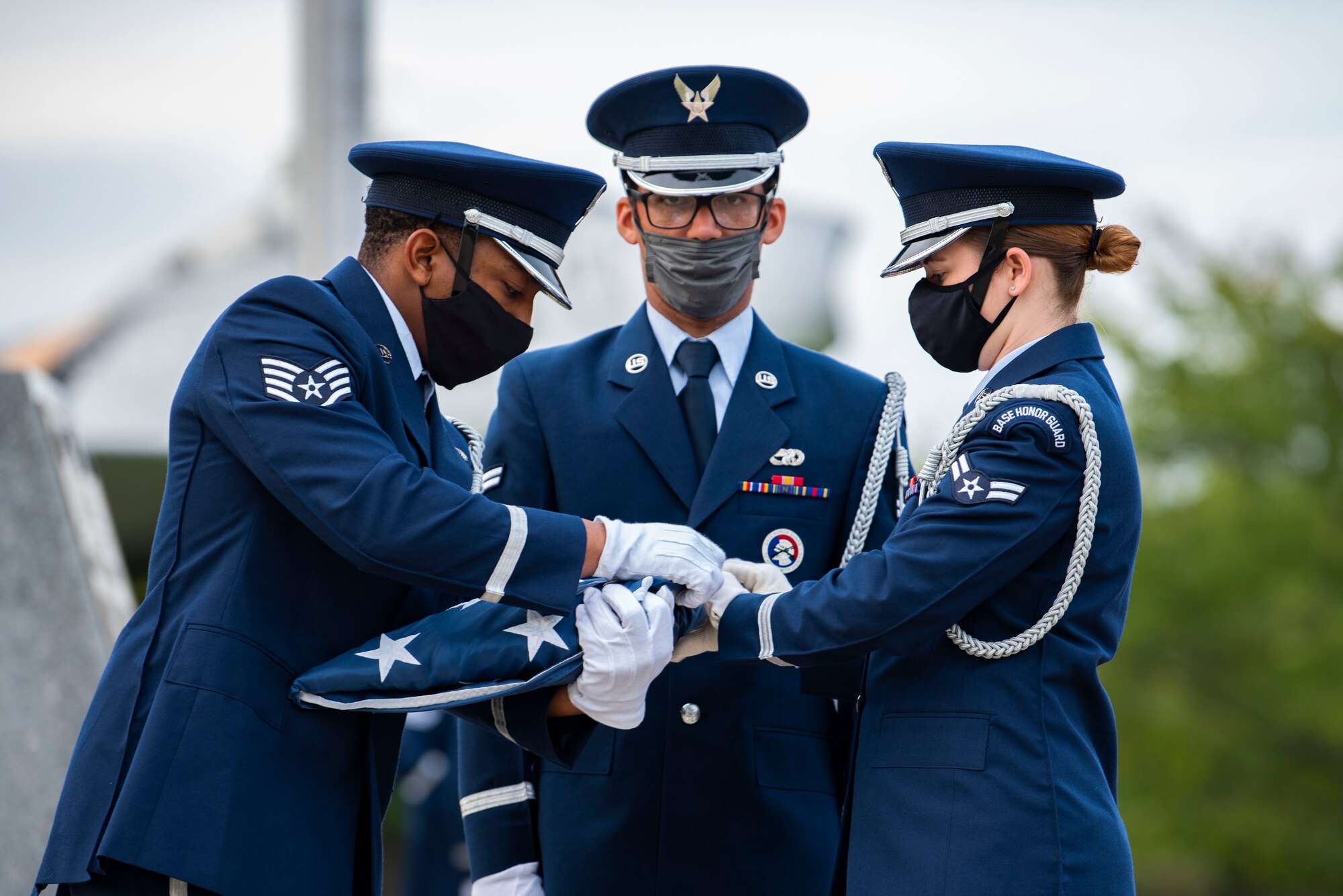 Military members in uniform fold an American flag.