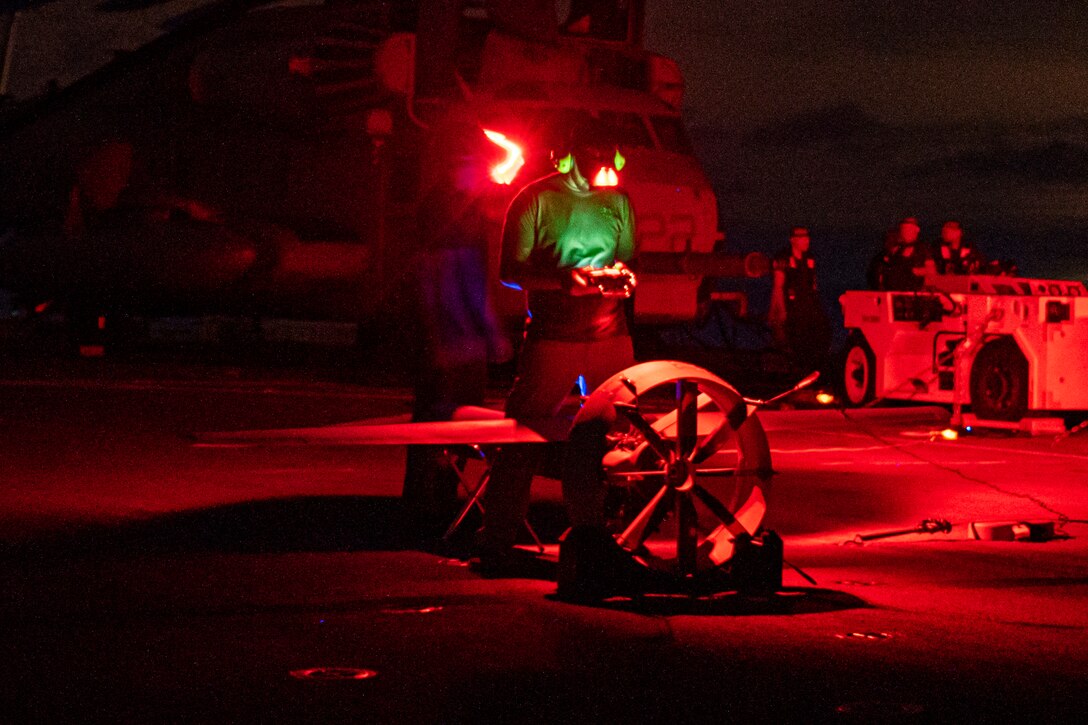 A Marine bathed in red light uses a device to check a small aircraft.