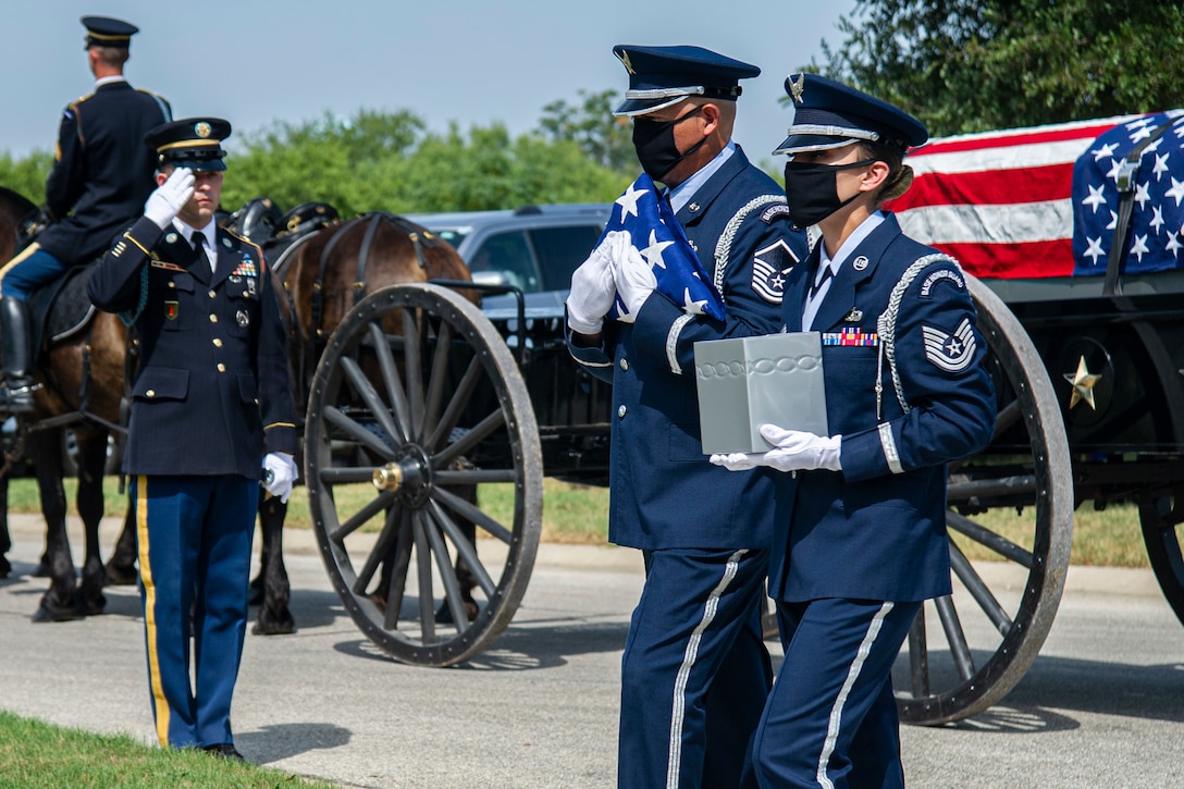 Two airmen carry  a small box and an American flag.