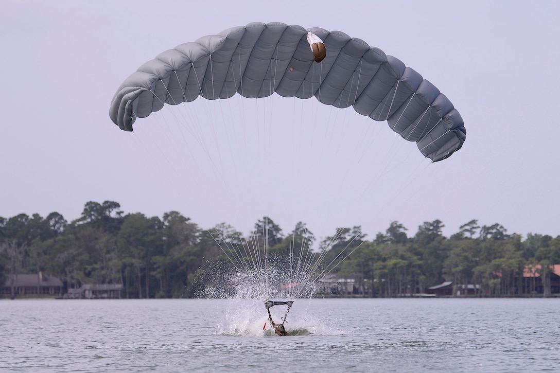 A soldier with an open parachute lands in a lake.