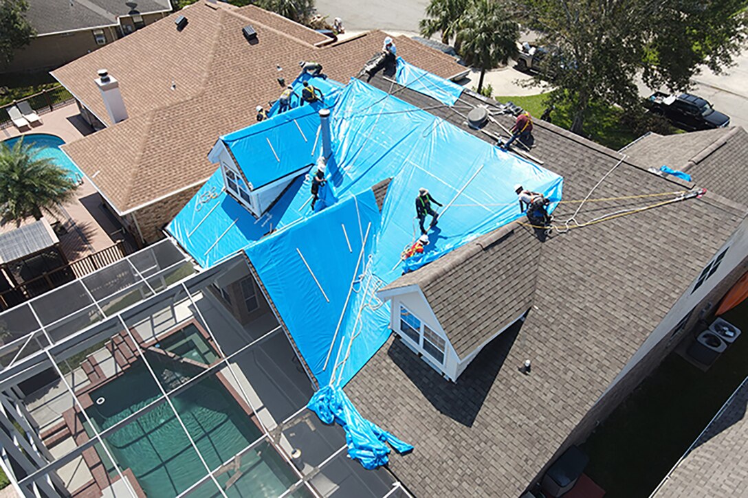 Workers install blue material on a roof.