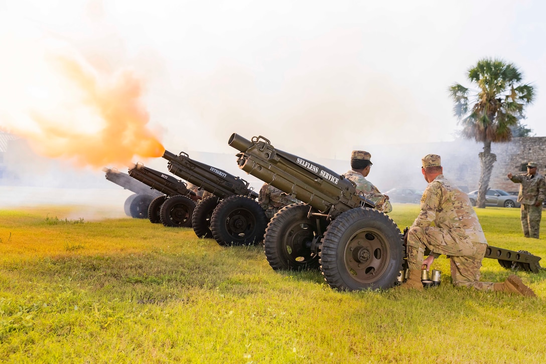 Soldiers fire cannons in a field.