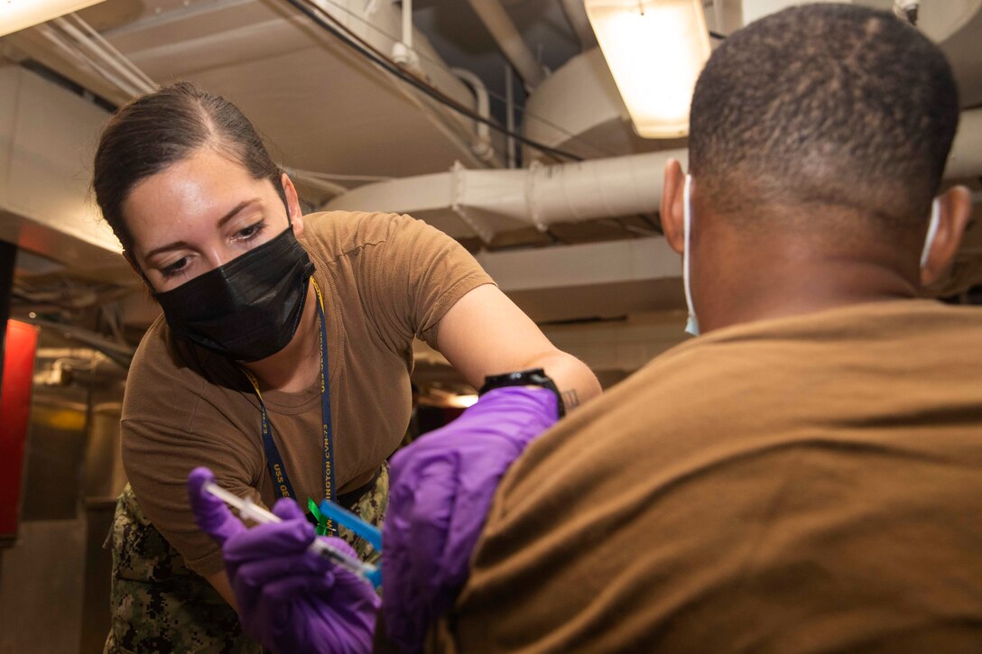 A sailor administers the COVID-19 vaccine to a fellow sailor.