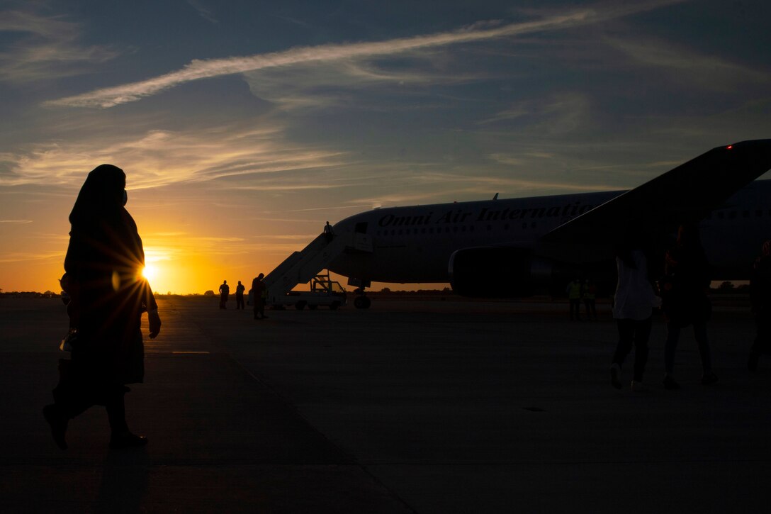Afghan evacuees walk towards an aircraft under a sunlit sky as shown in silhouette.