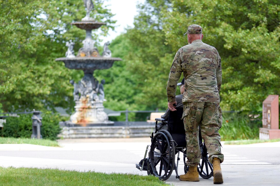 An airman pushes a person in a wheelchair.