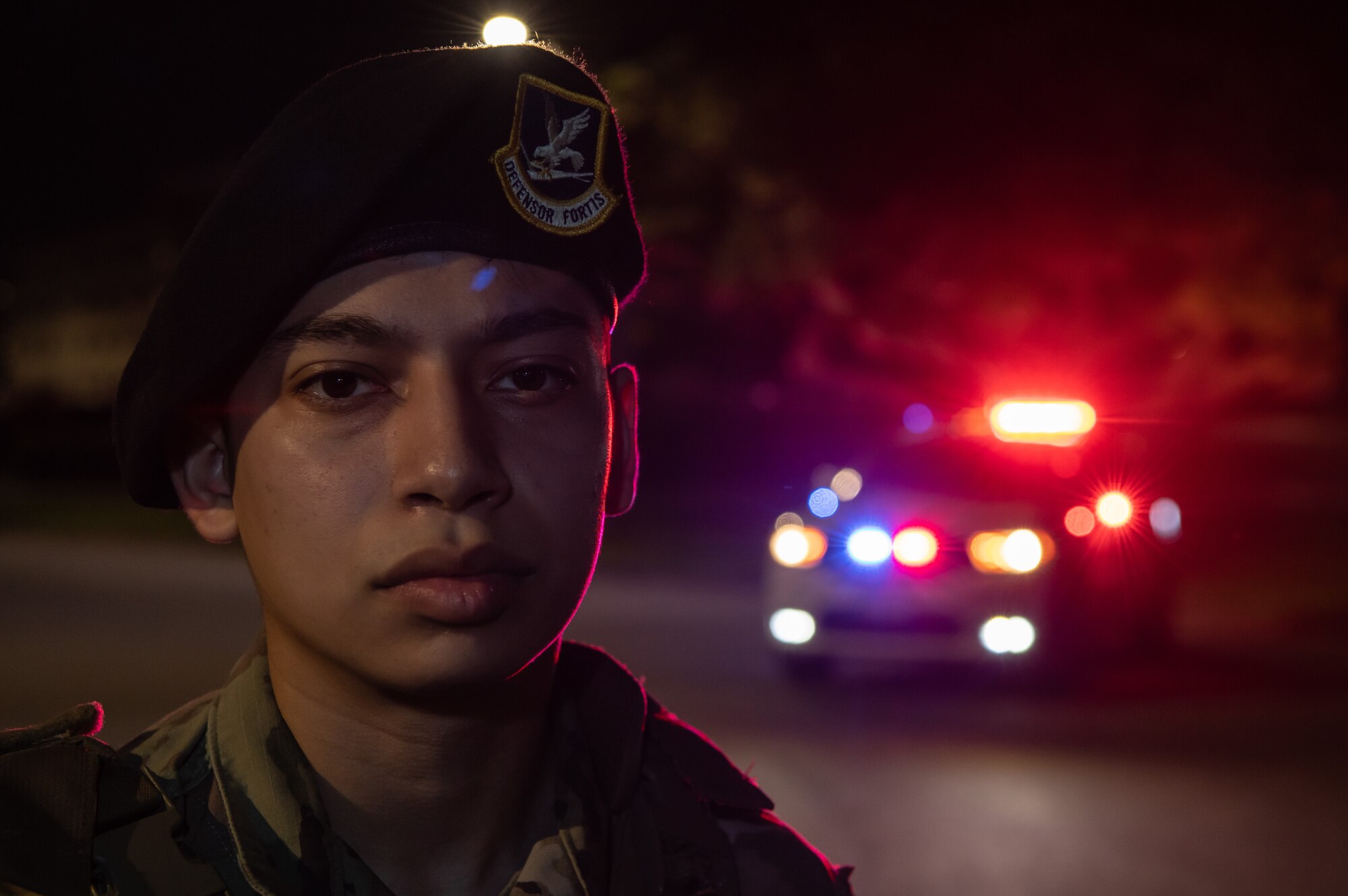 An Airman standing in front of a police car with the lights on.