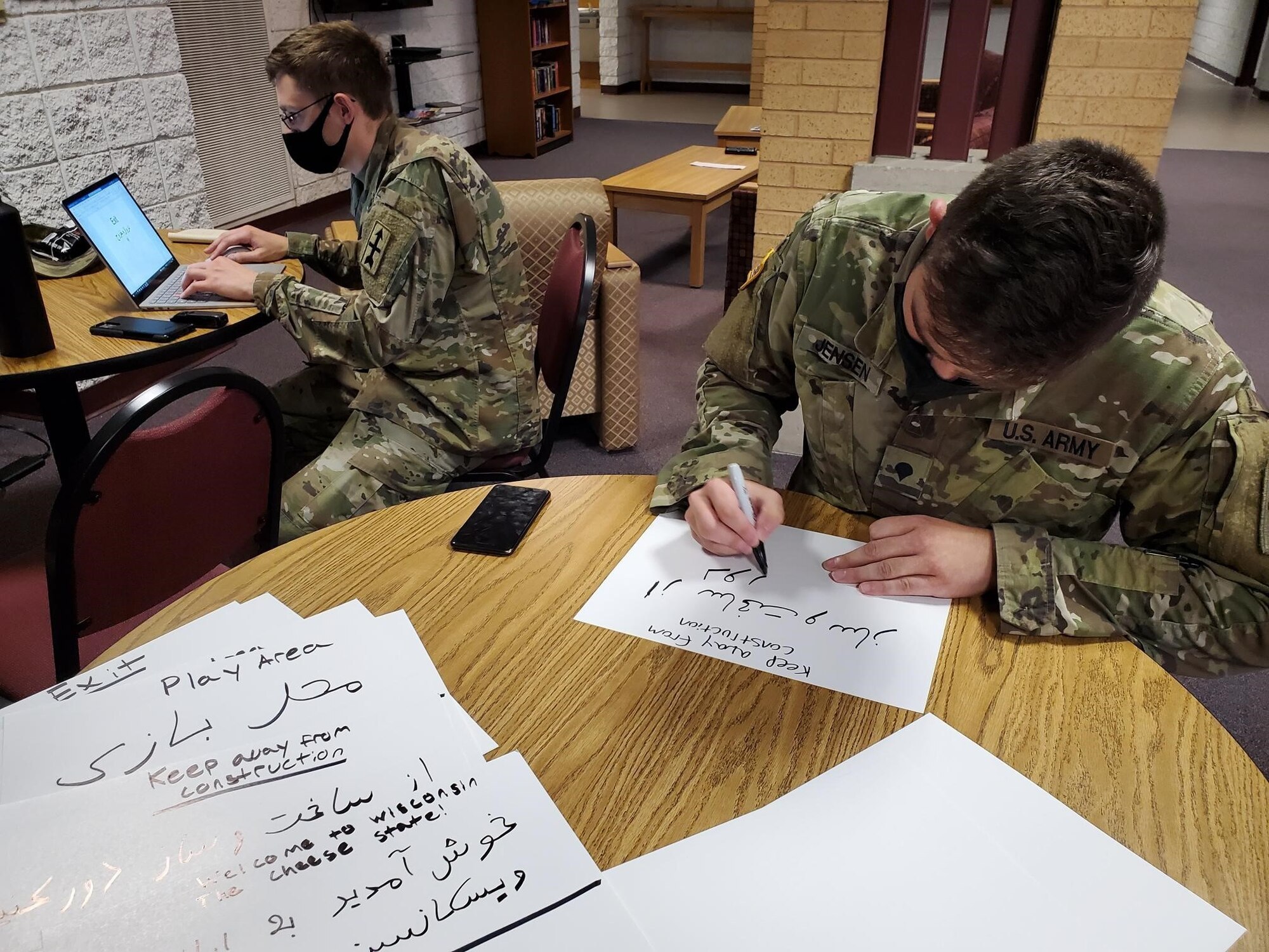 U.S. Army Cpl. Sean Jackett, left, and Spc. Zackary Jensen, Wisconsin Army National Guard linguists, create signs in Dari and Pashto, Aug. 25, 2021, to place in a welcome area for Afghan people arriving at Volk Field Combat Readiness Training Center near Camp Douglas, Wisconsin.
