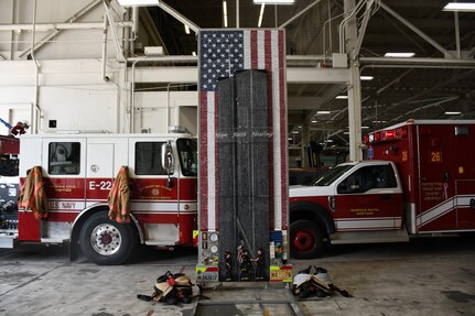 In the Navy Region Mid-Atlantic Fire and Emergency Services firehouse aboard Norfolk Naval Shipyard (NNSY) the “Divinity Among Heroes” memorial artwork stands in an ambulance bay. The tribute piece is made up of 30,000+ drywall and trim screws, 2,978 one-inch wooden blocks, the base, a simulated fire truck, is constructed of authentic gauges, cranks, handles, hoses, chevrons, and plates from a decommissioned fire truck and it stands 12 foot tall by four foot wide.