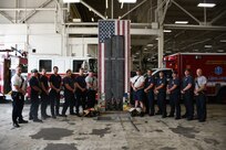 Members of the Navy Region Mid-Atlantic Fire and Emergency Services along with the Sept. 11 memorial tribute artwork designed by NNSY’s SurgeMain Sailor, Machinist Mate Chief Petty Officer (MMC) Joseph Pisano . The tribute piece is made up of 30,000+ drywall and trim screws, 2,978 one-inch wooden blocks, the base, a simulated fire truck, is constructed of authentic gauges, cranks, handles, hoses, chevrons, and plates from a decommissioned fire truck and it stands 12 foot tall by four foot wide.