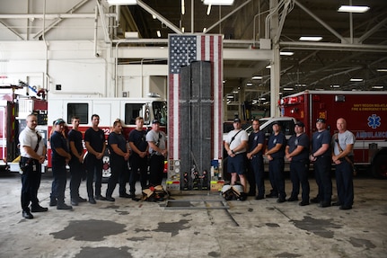 Members of the Navy Region Mid-Atlantic Fire and Emergency Services along with the Sept. 11 memorial tribute artwork designed by NNSY’s SurgeMain Sailor, Machinist Mate Chief Petty Officer (MMC) Joseph Pisano . The tribute piece is made up of 30,000+ drywall and trim screws, 2,978 one-inch wooden blocks, the base, a simulated fire truck, is constructed of authentic gauges, cranks, handles, hoses, chevrons, and plates from a decommissioned fire truck and it stands 12 foot tall by four foot wide.