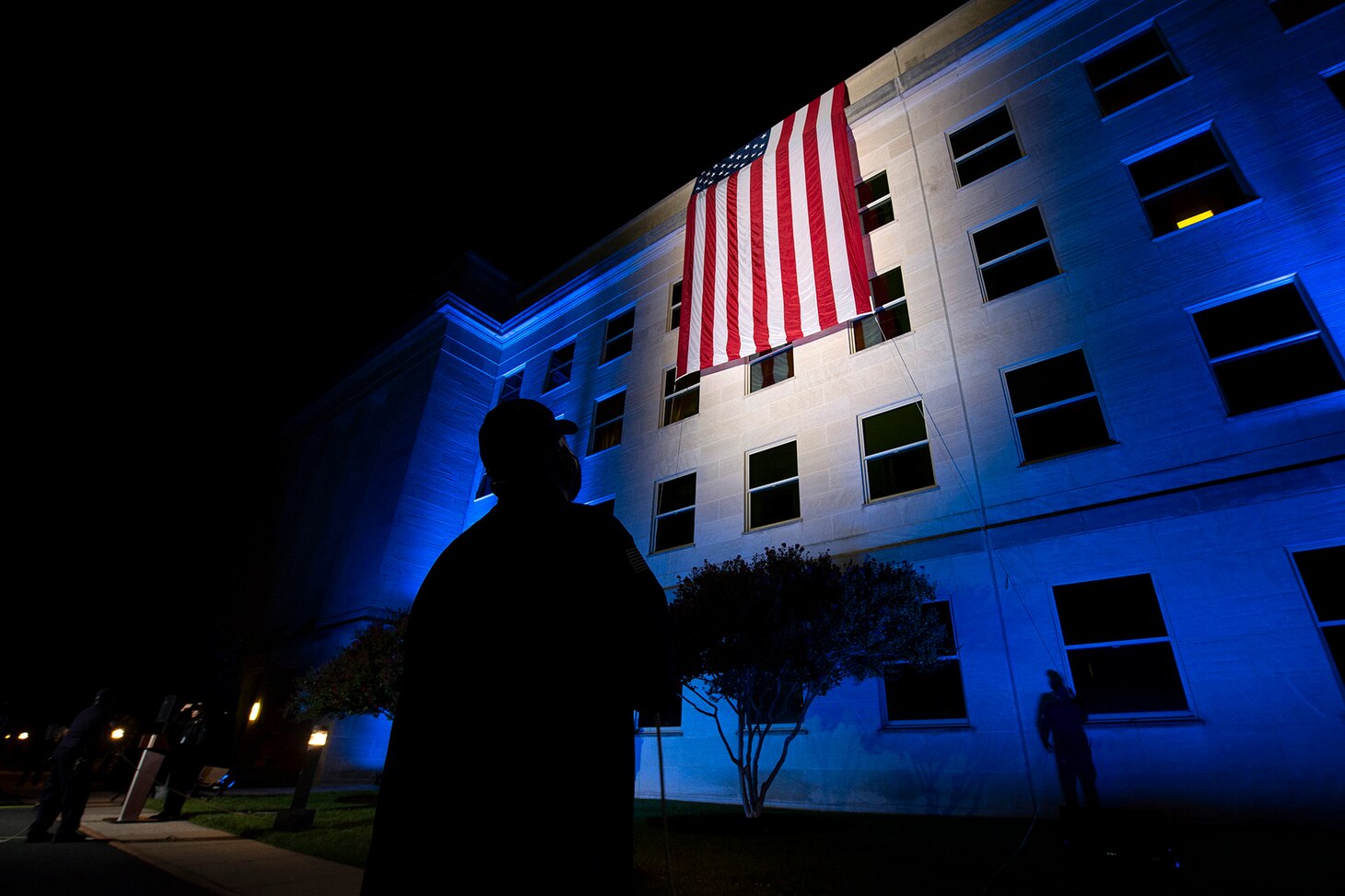 First responders guide an unfurling a flag over the side of the Pentagon before sunrise on the 20th anniversary of the 9/11 terrorist attacks.