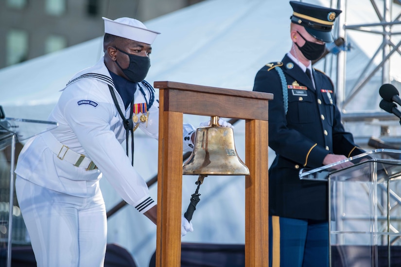 A sailor rings a bell while a soldier reads from a lectern.