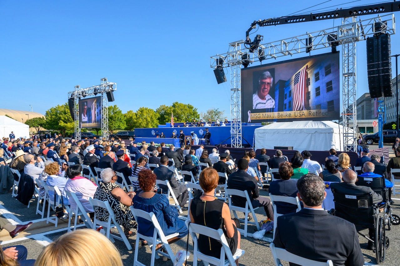 An audience watches a big screen in a parking lot.