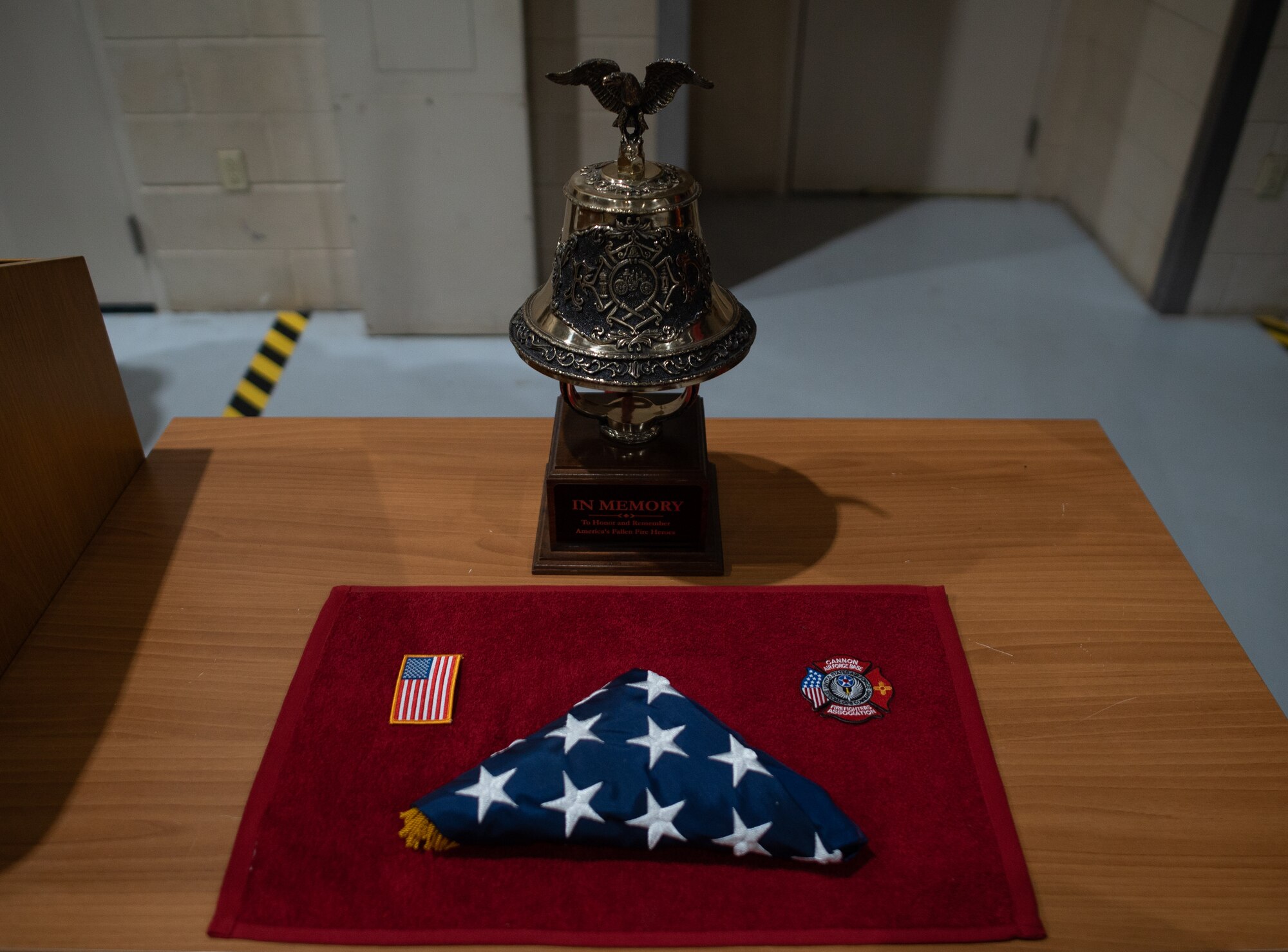 An American flag, patch, Cannon Air Force Base fire emergency services patch and ceremonial bell form part of a memorial to 9/11 during a ceremony at Cannon Air Force Base, N.M., Sep. 11, 2021. The memorial marked the 20th anniversary since the terrorist attacks on the United States in 2001 and included a nine-story stair climb in honor of the first responders who lost their lives responding to the attacks. (U.S. Air Force photo by Senior Airman Christopher Storer)