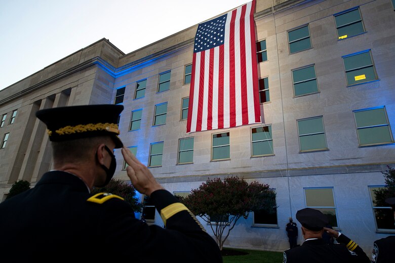 An officer salutes a large American flag hanging over the side of the Pentagon.