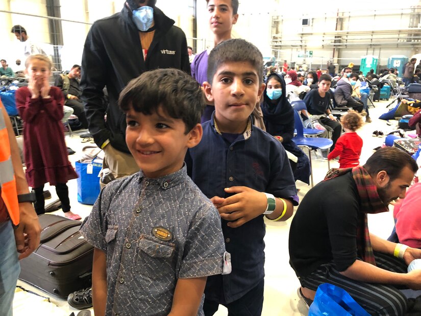 Two young boys smile while standing in a crowded room.