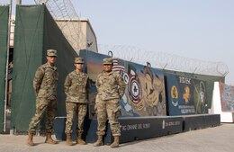 Spc. Miguel A. Martinez, Pvt. 1st Class Janice M. Salazar, and Spc. Onosai Misionare, Soldiers assigned to 3rd Expeditionary Sustainment Command, stand in front of T-walls painted by Soldiers in units who have previously served in 1st Theater Sustainment Command's operational command post at Camp Arifjan, Kuwait, on Sept. 10, 2021. The Fort Bragg, N.C., based Soldiers deployed in August to support 1st TSC's operational command post mission.
