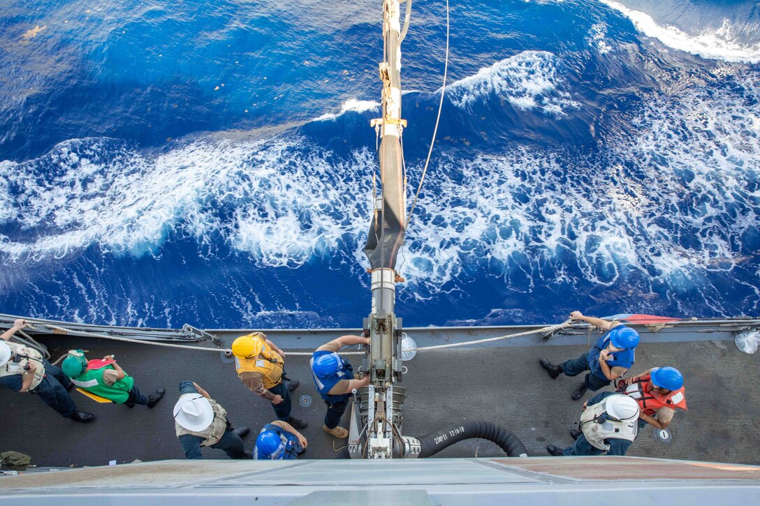 A look down at sailors as the secure a fuel pump on the edge of a ship.
