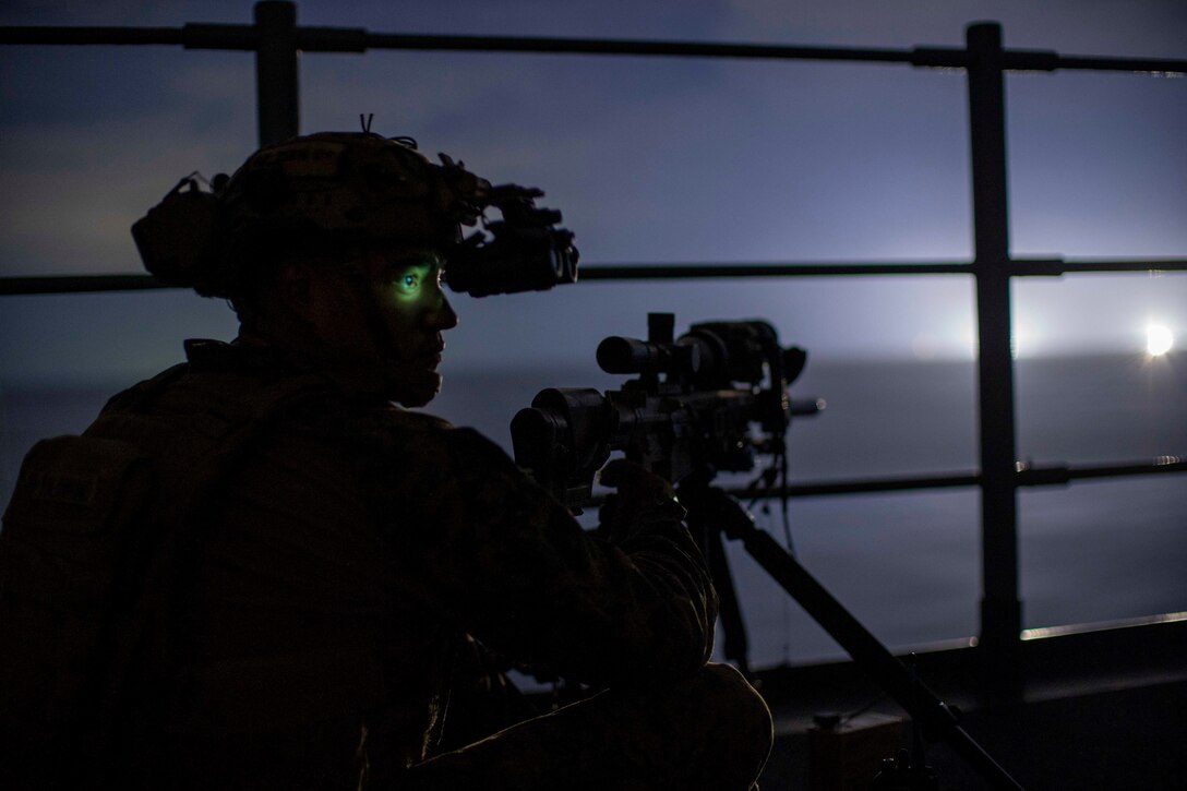 A Marine and his machine gun are silhouetted against a greyish sky.
