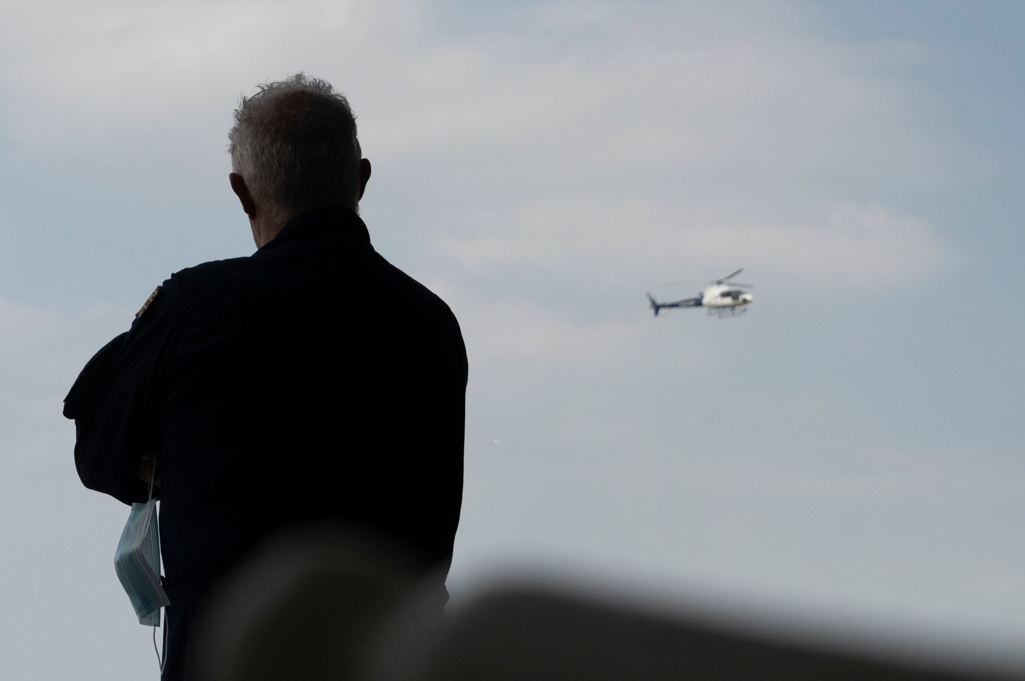 A man stand looking out at a helicopter in the sky.