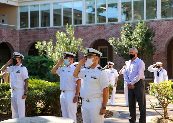 Naval Education and Training Command (NETC) staff members salute as tap plays at the end of a 9/11 memorial ceremony.