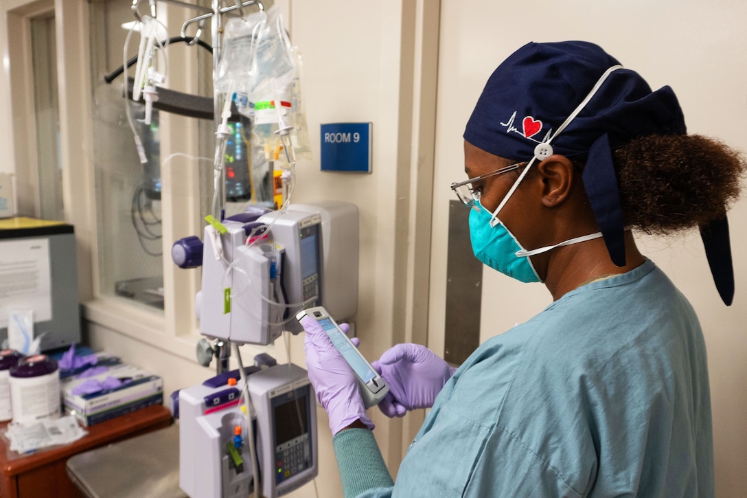 An airman wearing a face mask, gloves and medical gown prepares medical fluids to treat a patient.