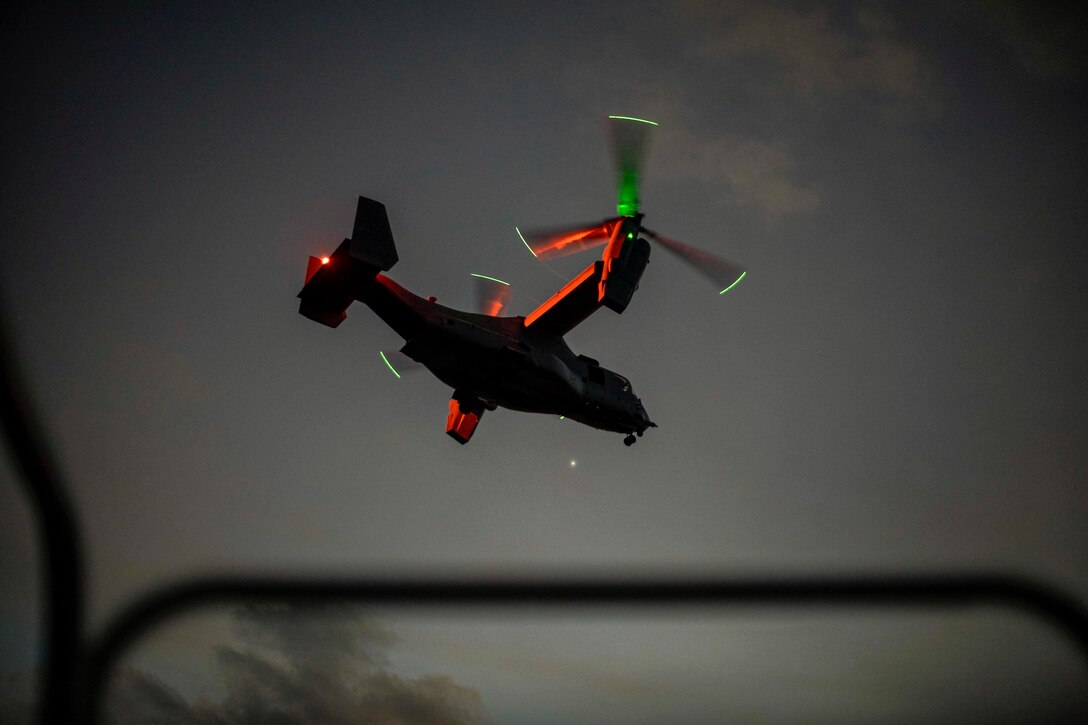 An aircraft flies in the dark illuminated by green and red lights.