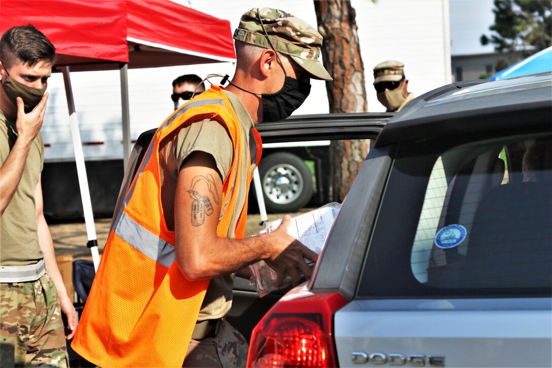 A soldier hands supplies to someone in a car.