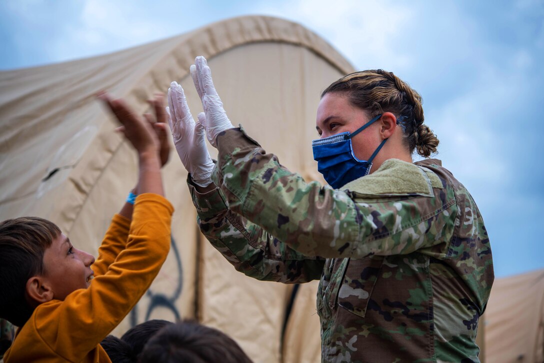 An airman gives high fives to a child with a tent in the background.