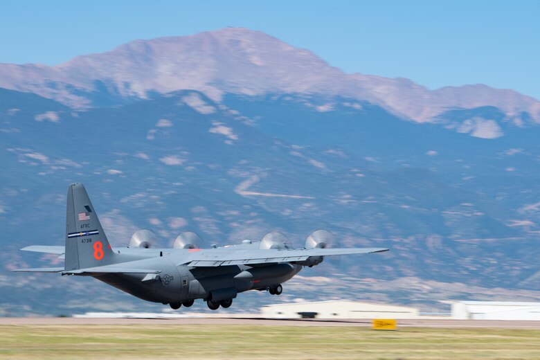 A C-130 with a large orange 8 on the tail takes off from a runway with a mountain range in the background.