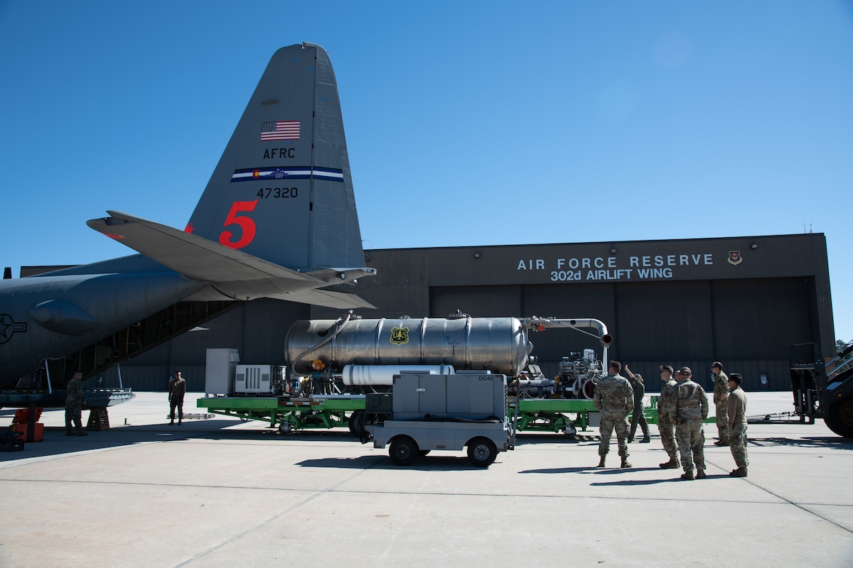 Airmen load a large metal storage unit with a U.S. Forest Service label on it into the back of a C-130 aircraft.