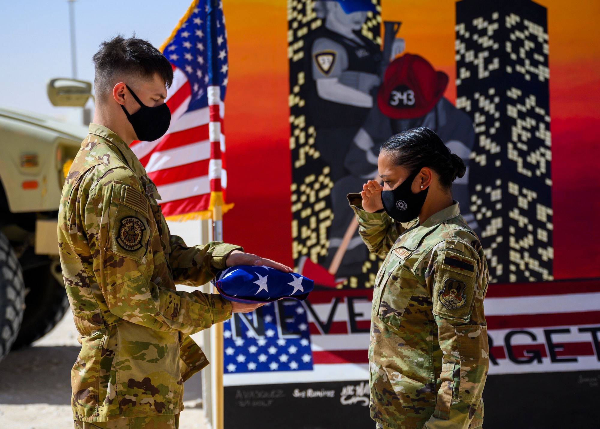 Staff Sgt. Aubrey Houston, 378th Expeditionary Security Forces Squadron defender, salutes the flag as it is held by Airman 1st Class Timothy Treat-Mass, 378th Expeditionary Civil Engineer Squadron firefighter, during a Remembrance Ceremony Sept. 11, 2021, at Prince Sultan Air Base, Kingdom of Saudi Arabia.