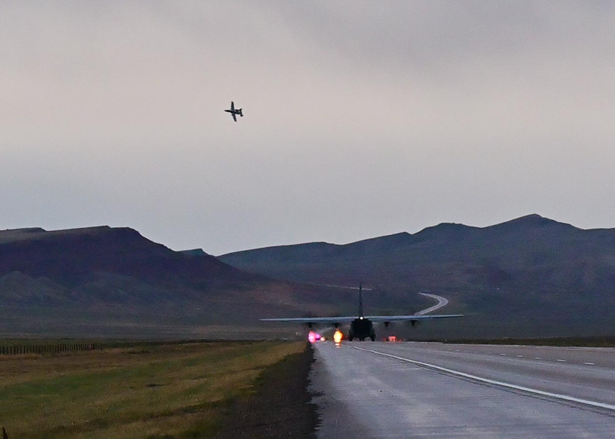 A fighter aircraft in the air above a cargo reversing down a highway