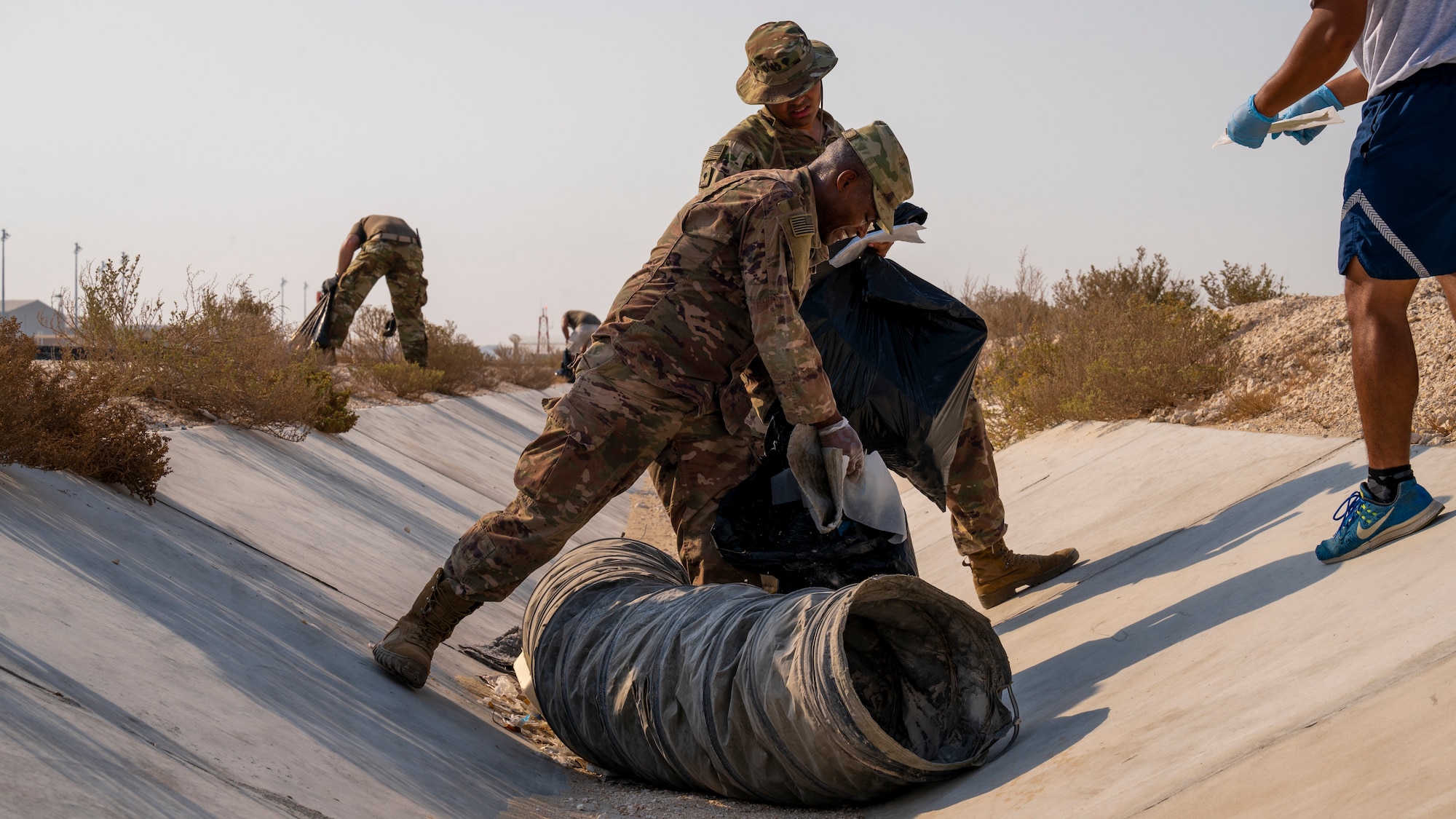 Soldiers pick up foreign object debris in a drainage ditch near the flightline Sept. 8, 2021, at Al Udeid Air Base, Qatar.