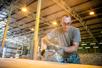 U.S. Air Force Tech. Sgt. Brandon Mullenix, 420th Munitions Squadron conventional maintenance section chief, cuts a piece of wood with an electrical saw prior to an asset transport at RAF Welford, England, Sept. 7, 2021. Airmen from the 420th MUNS constructed multiple wooden structures and supports to help stabilize inert assets to be transported to RAF Lakenheath for an upcoming Agile Combat Employment exercise. (U.S. Air Force photo by Senior Airman Eugene Oliver)