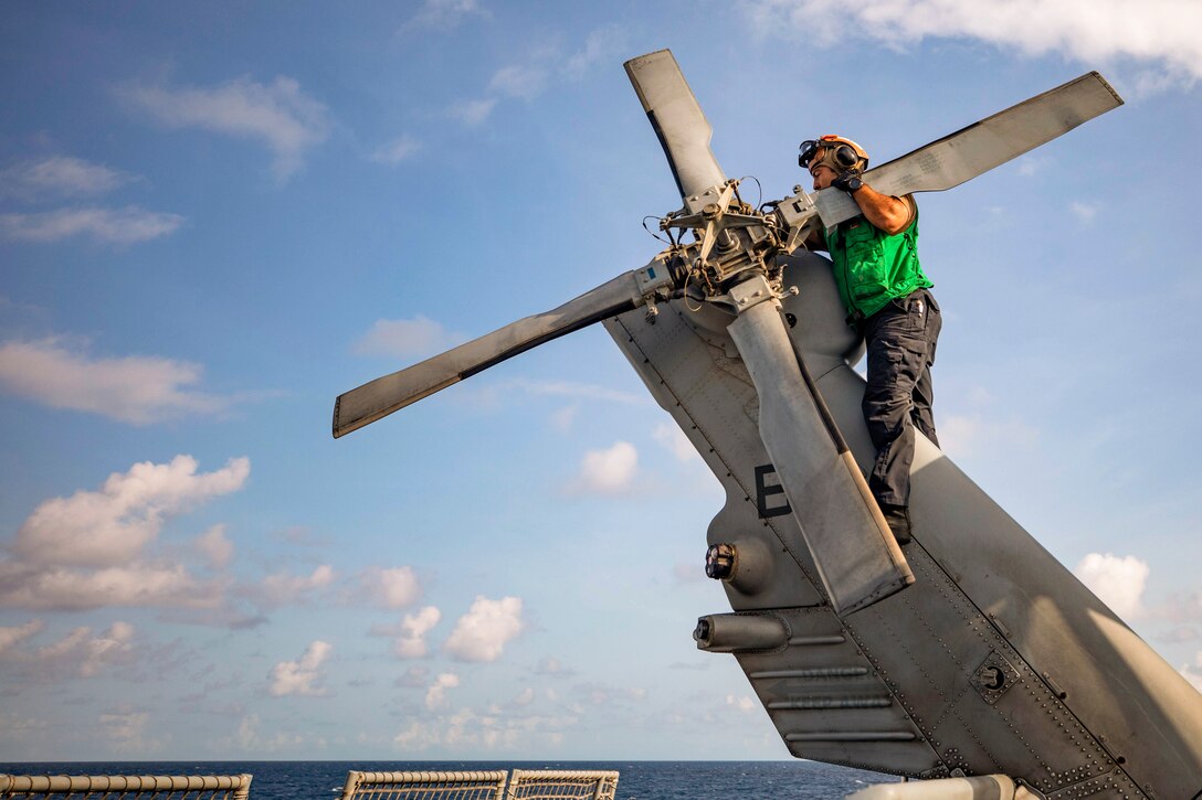 A sailor works on the propeller of a helicopter parked on a ship at sea.