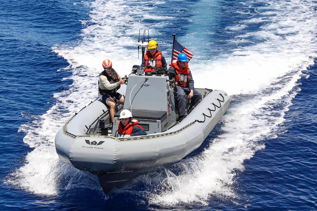 Four sailors ride in an inflatable boat flying the American flag.