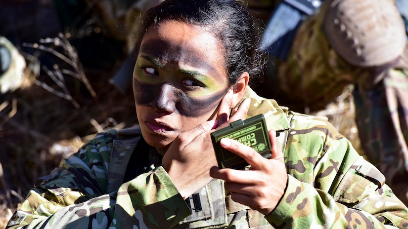A soldier applies camouflage facepaint during a sunny day.