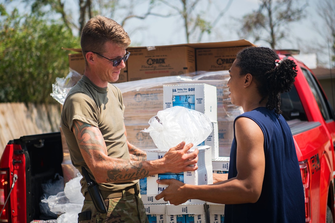 A soldier hands over a  case of water and a bag of ice to a resident.