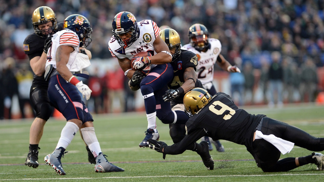 Army  players tackle Navy player on football field.