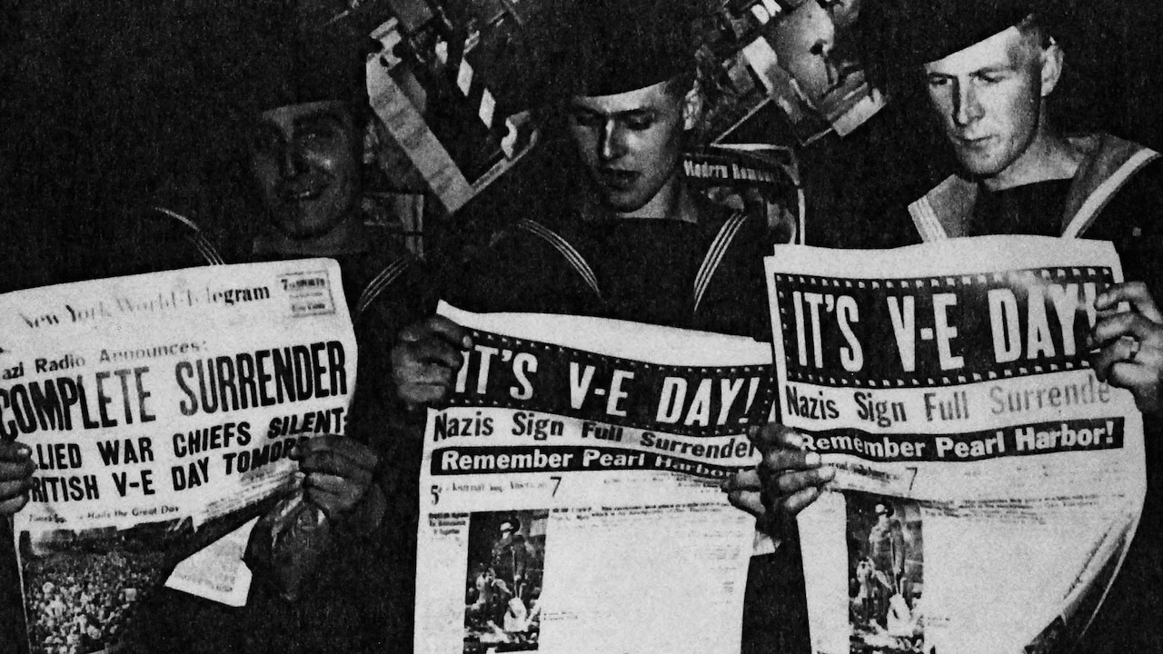 Troops reading newspapers announcing V-E Day