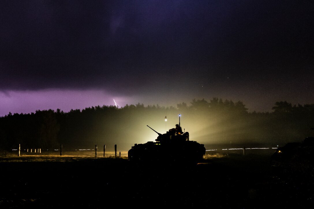 A military vehicle parked at night as lightning strikes in the background.