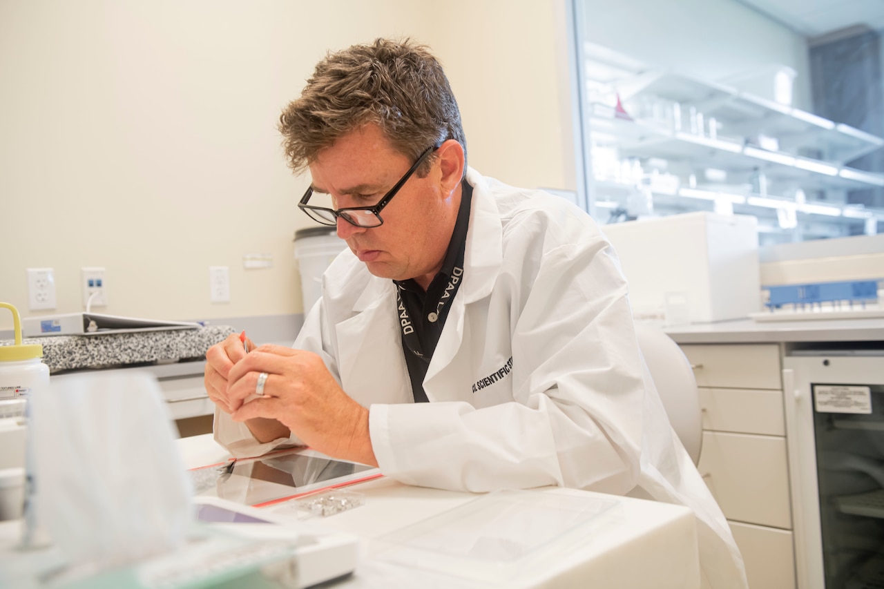 A man wearing a lab coat examines something in his hands.