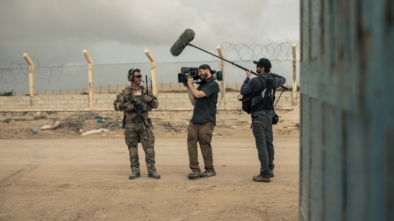 Camera person films person in uniform in desert-like setting.