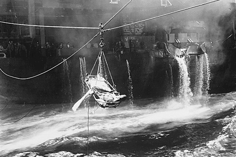 A wounded sailor is suspended above choppy seas during a ship-to-ship transfer.