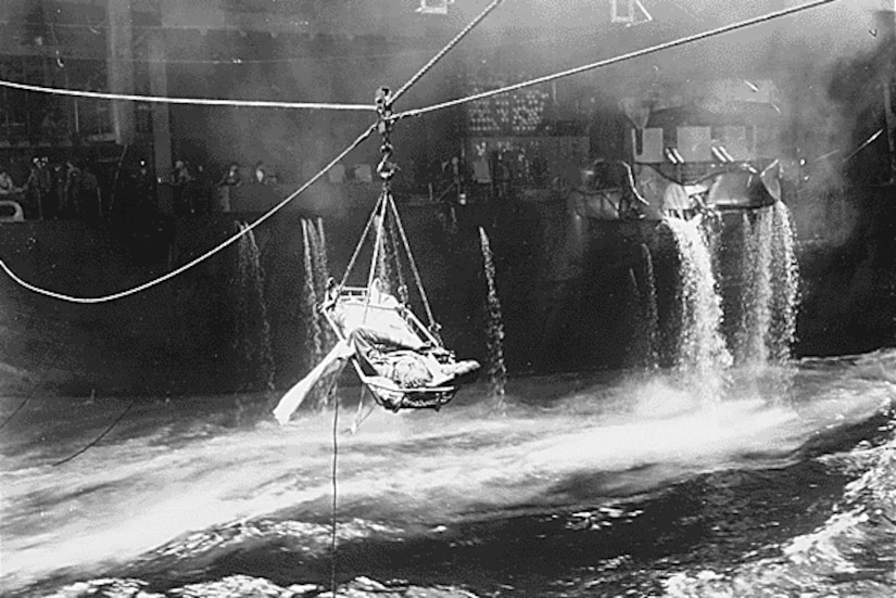 A wounded sailor is suspended above choppy seas during a ship-to-ship transfer.