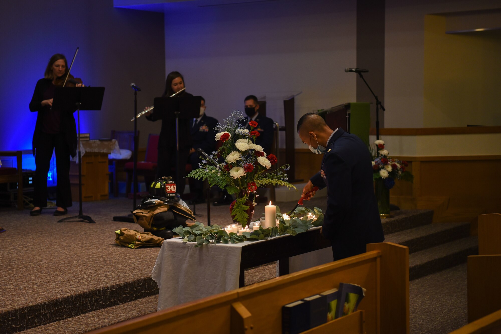 A military chaplain lights a candle while a flute and a violin are being played in the back
